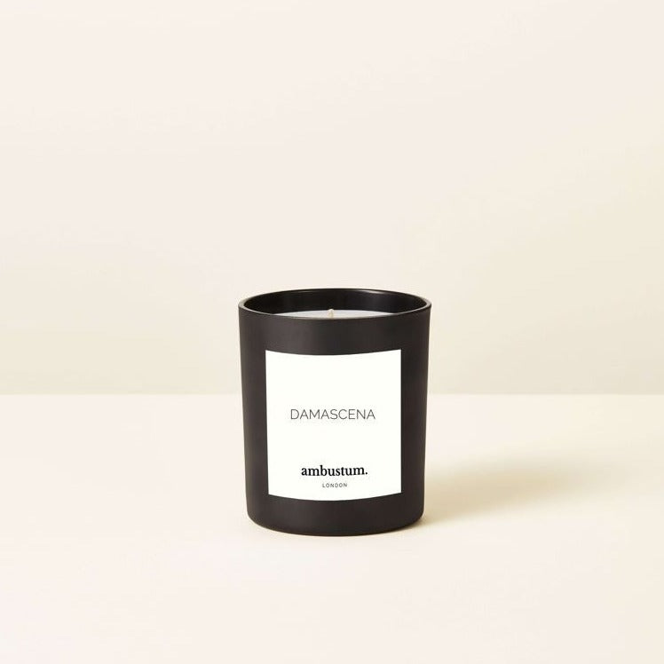 An ambustum candle with scent notes of luxurious fragrance experience, blending sweet and fruity notes of blackcurrant, damson plum, and mandarin with delicate floral scents of carnation, rose, lily, and geranium. The base notes of warm amber, creamy sandalwood, and cedarwood create a seductive and romantic ambiance. Presented in a black glass jar with luxurious yet simplistic labelling.